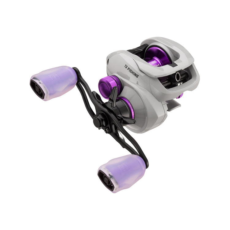 A gray fishing reel with purple accents, featuring two large purple-handled grips on a black double handle. The reel has a modern design with visible cogs and a glossy finish.