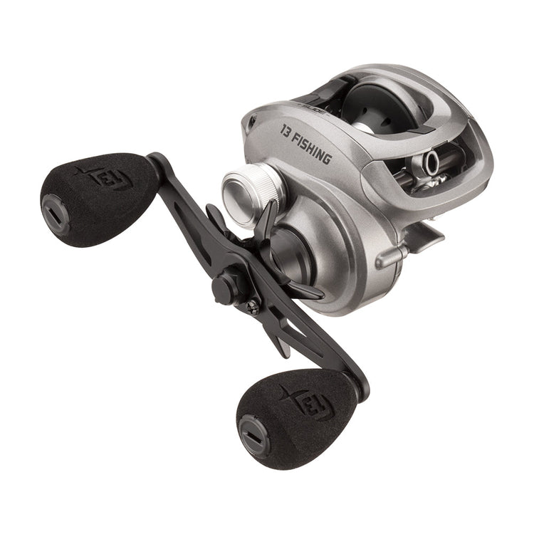 A silver fishing reel with black handles, featuring the brand name "13 Fishing". The design is sleek and compact, suitable for baitcasting.