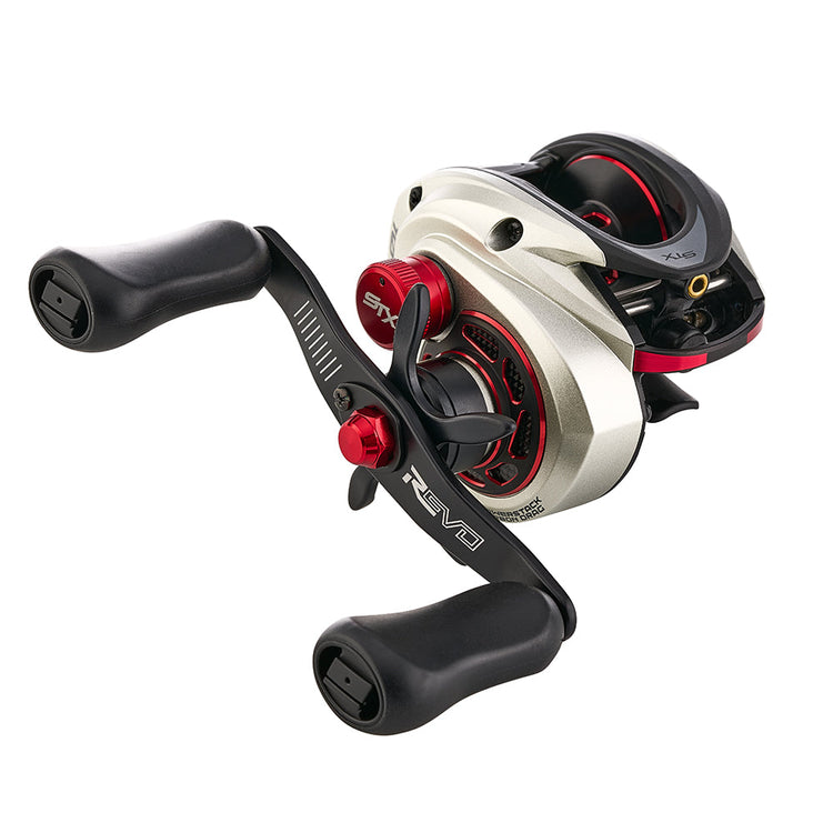 A silver and red baitcasting fishing reel with black ergonomic handles and detailed mechanical components is shown against a white background.