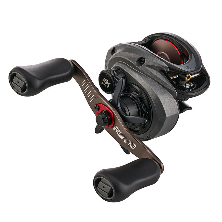 A silver and black fishing reel with two ergonomic handles, featuring a sleek design and a red accent near the crank. The reel has visible dials and a textured grip.