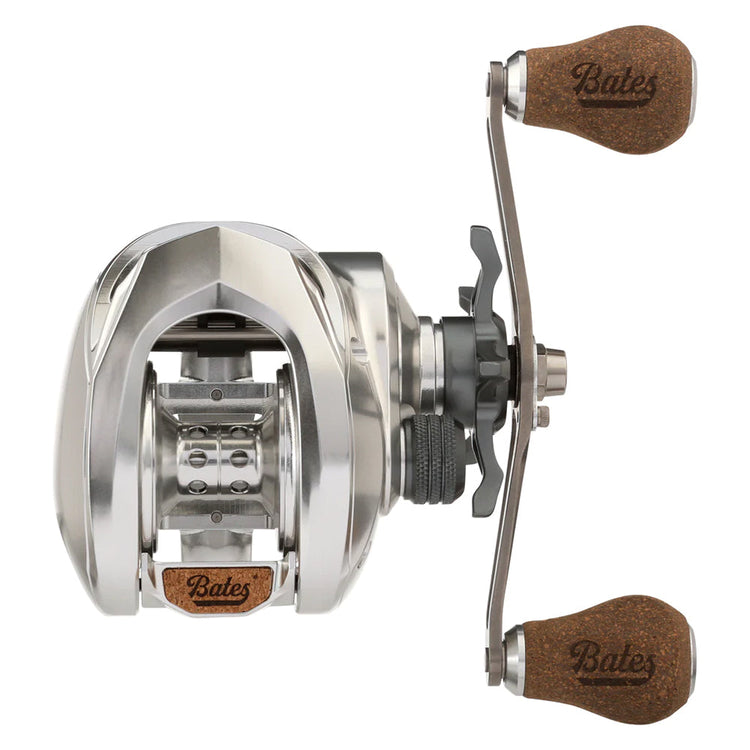 A silver baitcasting fishing reel with a metallic finish, featuring two brown cork handles marked "Bates." The reel shows a detailed, robust design with visible gearing and mechanics.