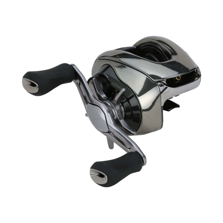 A silver baitcasting fishing reel with two black handles. The sleek design has a metallic finish and engravings on the casing. The reel appears compact and modern, suitable for fishing enthusiasts.