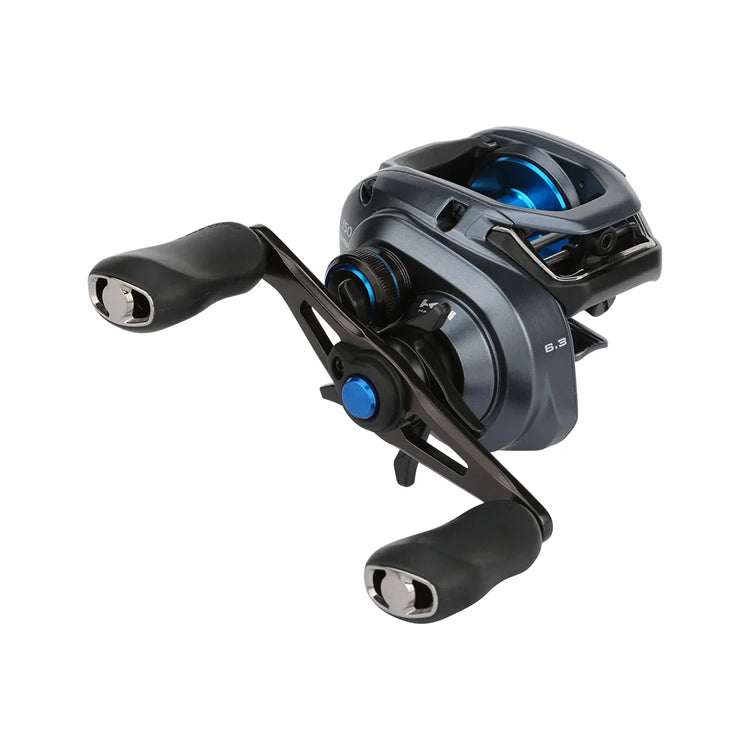 A close-up of a modern fishing reel with a sleek design. It features a metallic gray body with black handles and blue accents. The reel displays numbers indicating gear ratio settings.