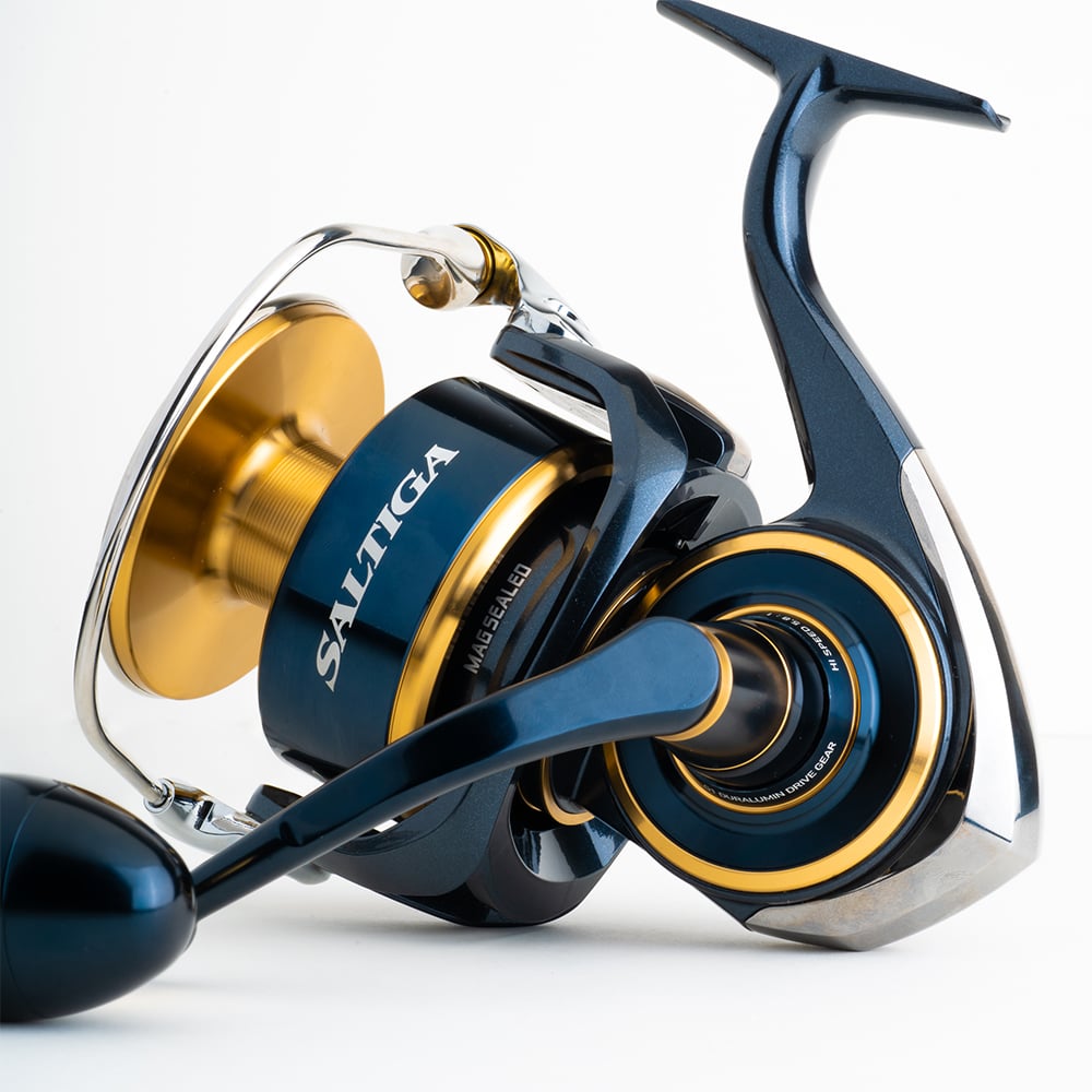 A close-up of the Daiwa Saltiga Spinning Reel 8000H highlights its dark blue and gold finish with intricate details and a modern design. The Monocoque Body stands out, emphasizing its durability and strength against a plain, light background.