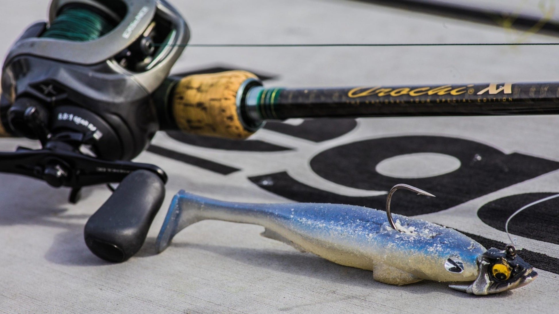 A Megabass fishing rod with a green and black reel rests on a gray surface. In front of the rod is the Megabass Body Balance Swimbait Jighead, a lifelike blue and gray fish-shaped lure designed for stable swimming action, complete with a hook. The background features bold black lettering.