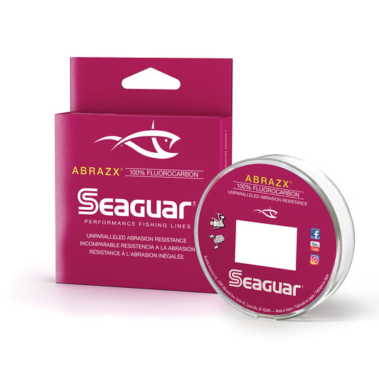 A magenta box and spool of Seaguar AbrazX Fluorocarbon Line feature a white fish logo and text highlighting "unparalleled abrasion resistance," ideal for heavy cover. The spool matches the branding, catering to avid anglers.