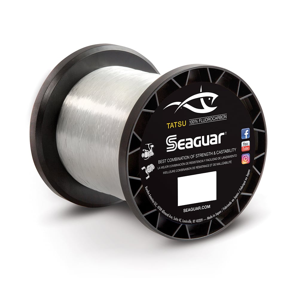 A spool of Seaguar Tatsu Fluorocarbon Line, produced by Seaguar and manufactured with a double-structure process, showcases a black label that includes a fish logo alongside social media icons. The line is neatly coiled around the upright-standing spool.