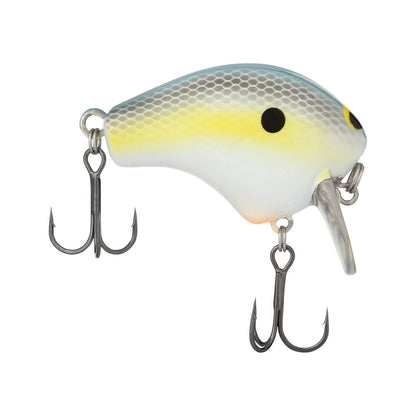 A close-up of a Shimano Macbeth Shallow 50F Wake Bait, designed to resemble a small fish. This wake bait showcases a white body with a light yellow stripe and black dot, equipped with two metal treble hooks hanging from the bottom, and features a clear plastic lip at the front for precise action.