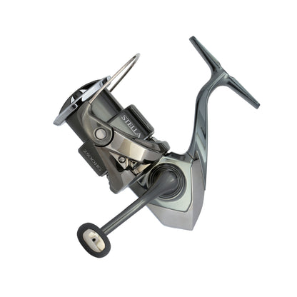 The Shimano Stella FK Spinning Reel 1000FK by americanlegacyfishing features a sleek silver and black design with MicroModule II technology for smooth performance. Its ergonomic handle and modern metallic finish ensure durability, all showcased against a plain white background.