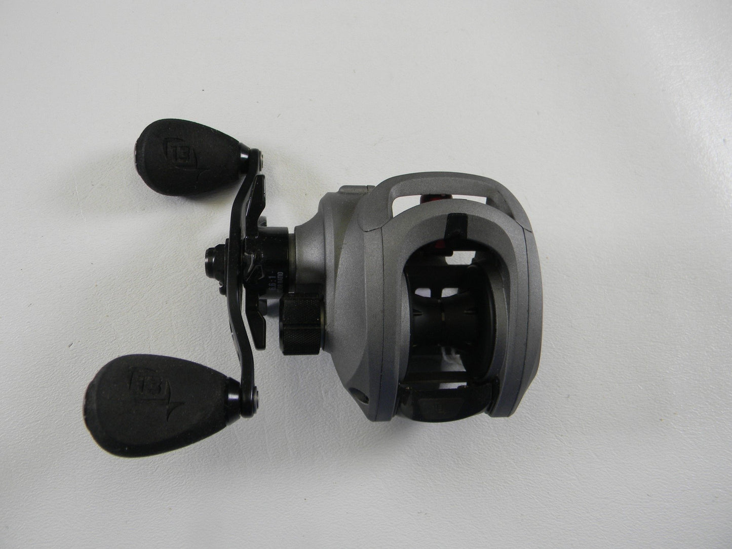 The 13 Fishing Inception IN6.6LH 6.6:1 LH, shown against a white background, is a used gray baitcasting reel featuring black rubber grips on the handle, a compact design, and a smooth metallic finish. It's perfect for those looking to trade in gear for store credit through the Rod and Reel Trade-In Program.