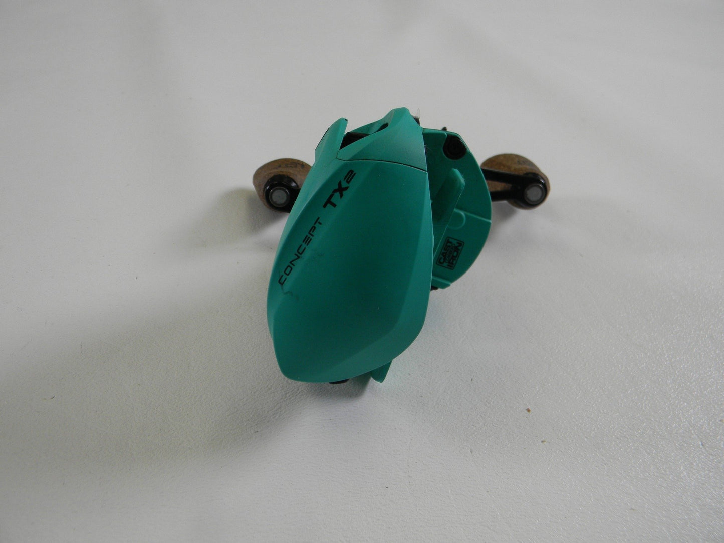 The 13 Fishing Concept TX2 TX2-7.5-LH, a teal used casting reel in very good condition, sits on a white surface. Its compact design is highlighted with close-up details of the spool and handle, and it’s eligible for store credit or Rod and Reel Trade-In.