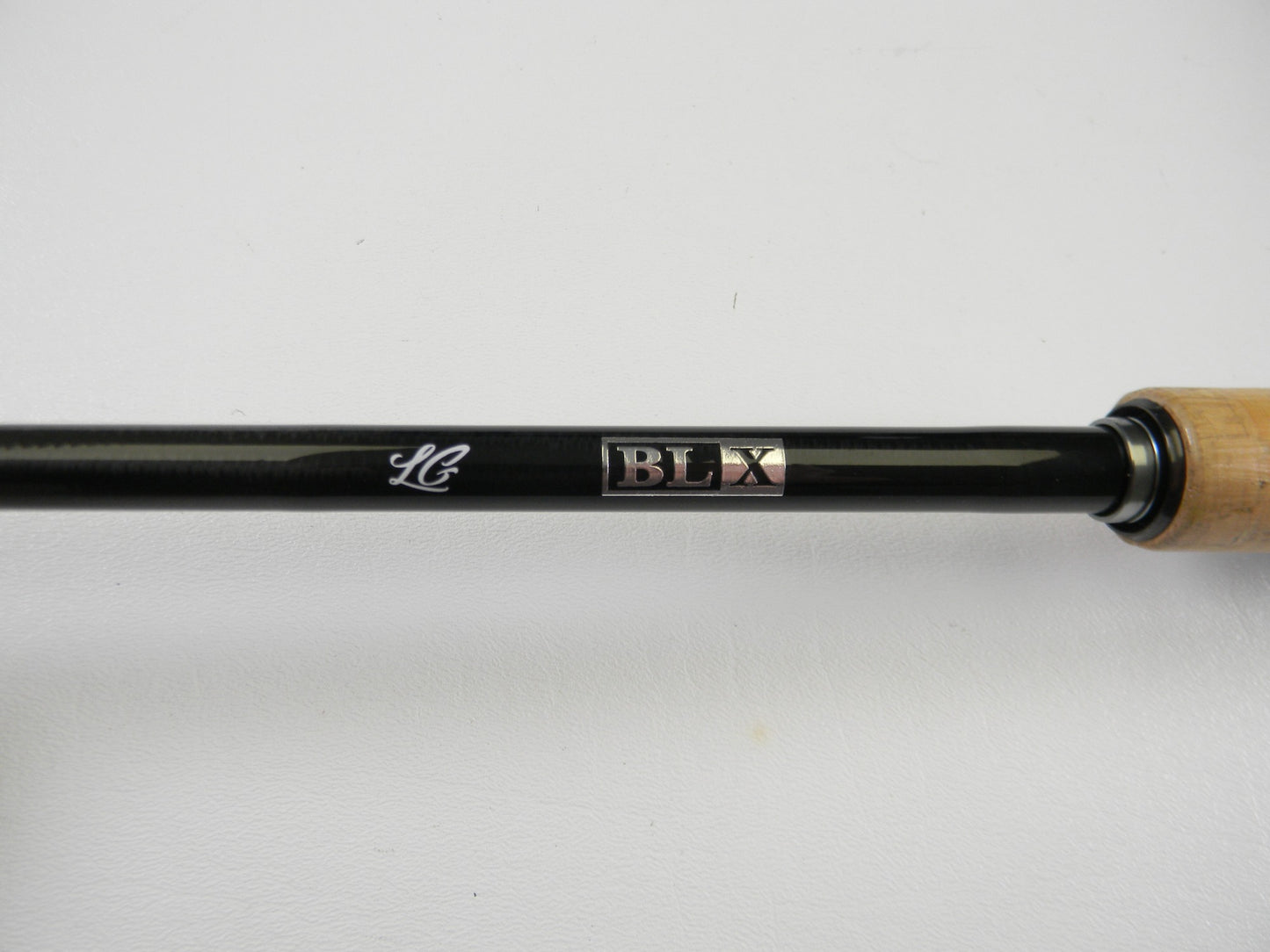 Close-up of a black Daiwa BLXLG731MLFB 7'3" Medium Light casting rod's wooden grip handle on the right. Its "LC" and "BLX" markings indicate premium design, ideal for upgrading through our Rod and Reel Trade-In Program. Background is plain white.