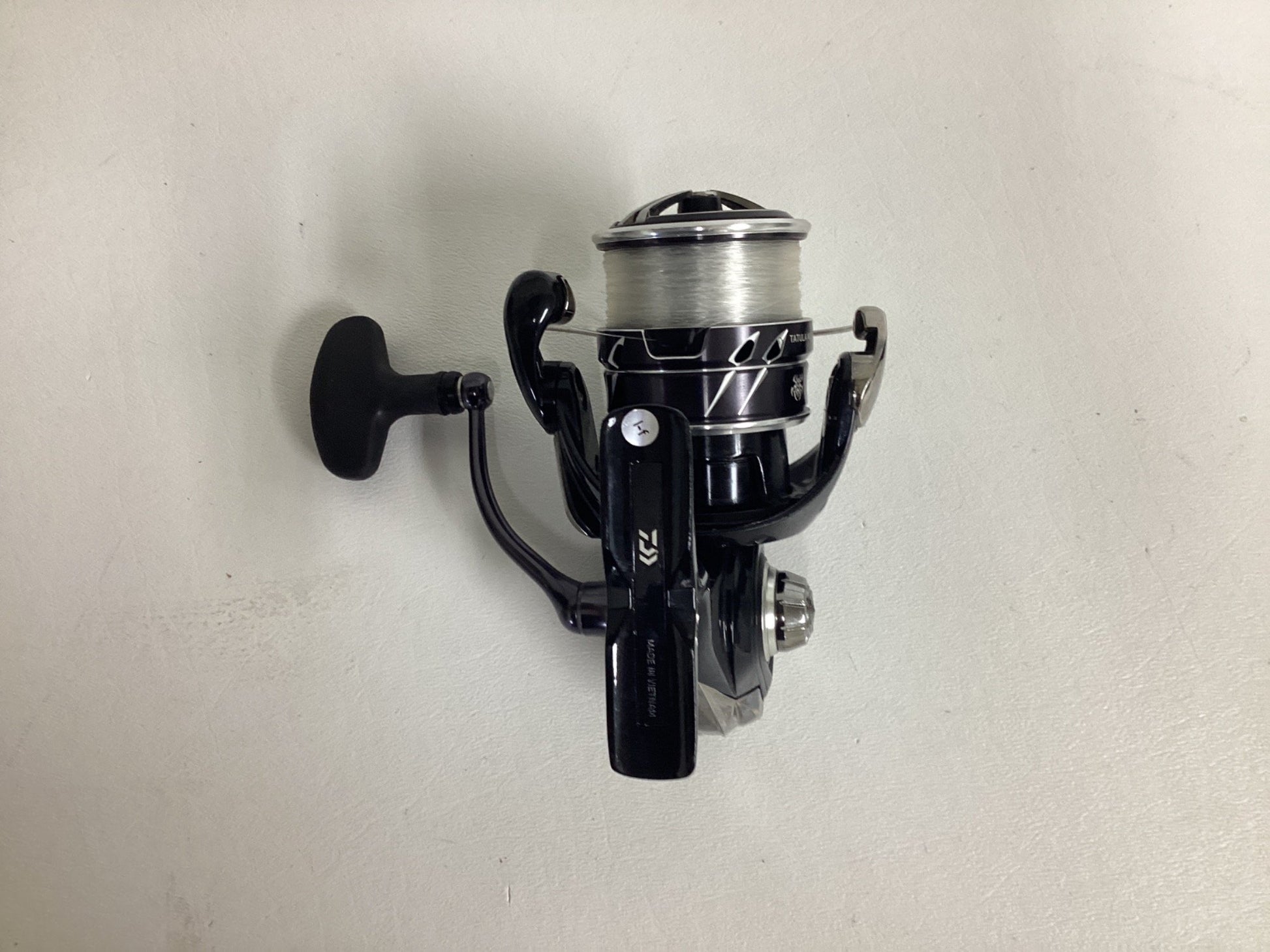 The Daiwa Tatula MQ LT3000-CXH 6.2:1 spinning reel in excellent condition, loaded with fishing line, sits elegantly against a white background. Ideal for those considering the Rod and Reel Trade-In Program to exchange used gear for store credit.