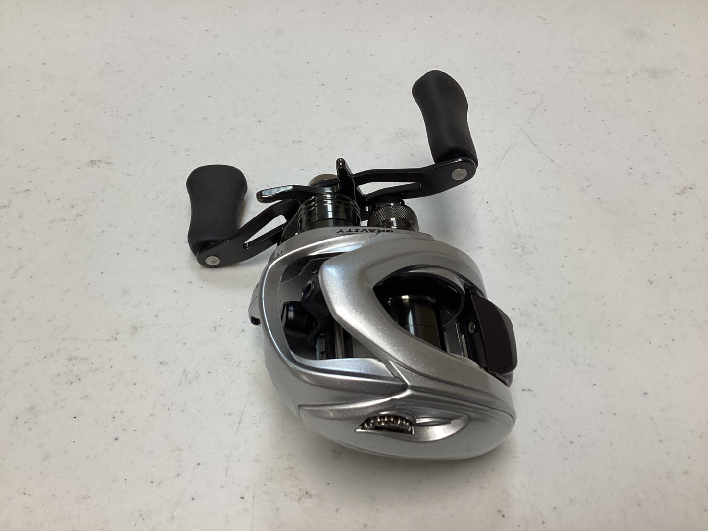 The Ark Gravity 7 G7107 Reel, in excellent condition with silver finish and black handles, is ready on a white surface for the Rod and Reel Trade-In program where used gear can earn valuable store credit.