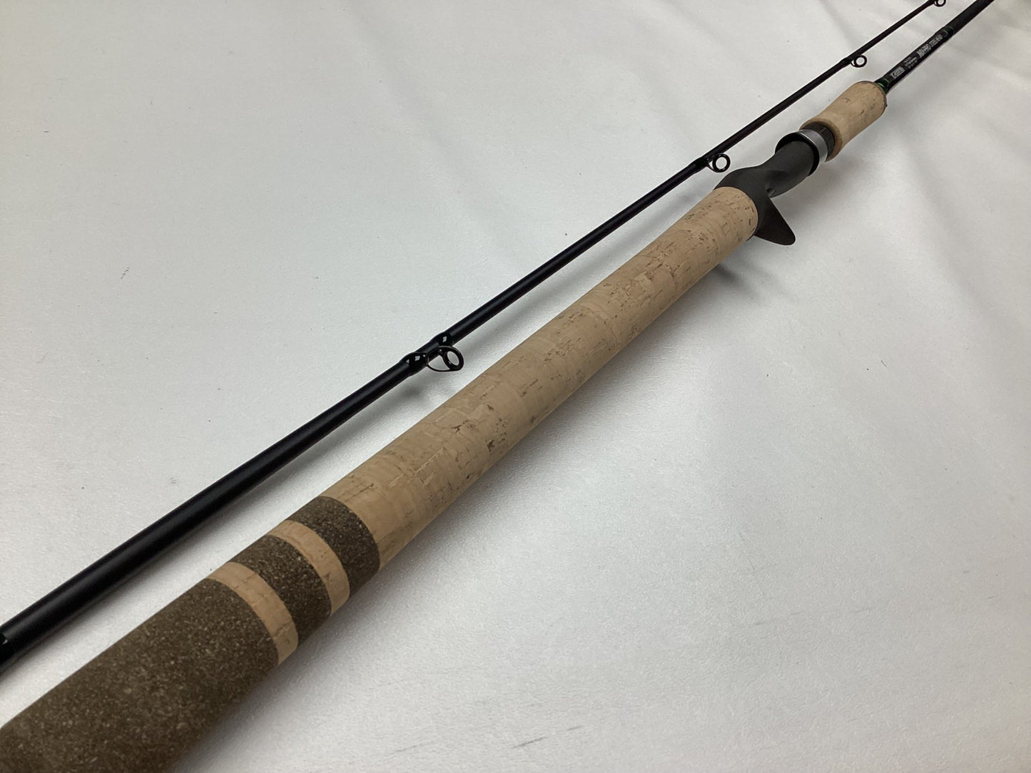 A G. Loomis IMX-PRO Steelhead Casting Rod 1023-2C STR 8'6" Medium Heavy, in mint condition, lies on a white surface. With its sleek black finish, cork handle with darker rings, and metal guides, it's ideal for the Rod and Reel Trade-In Program to upgrade your gear.