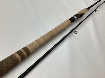 A G. Loomis IMX-PRO Steelhead Bead 1201-2S STBR 10'0" Medium Light spinning rod in mint condition, featuring a long beige cork handle, black reel seat, and partial black shaft with three line guides, is laid out on a white surface.