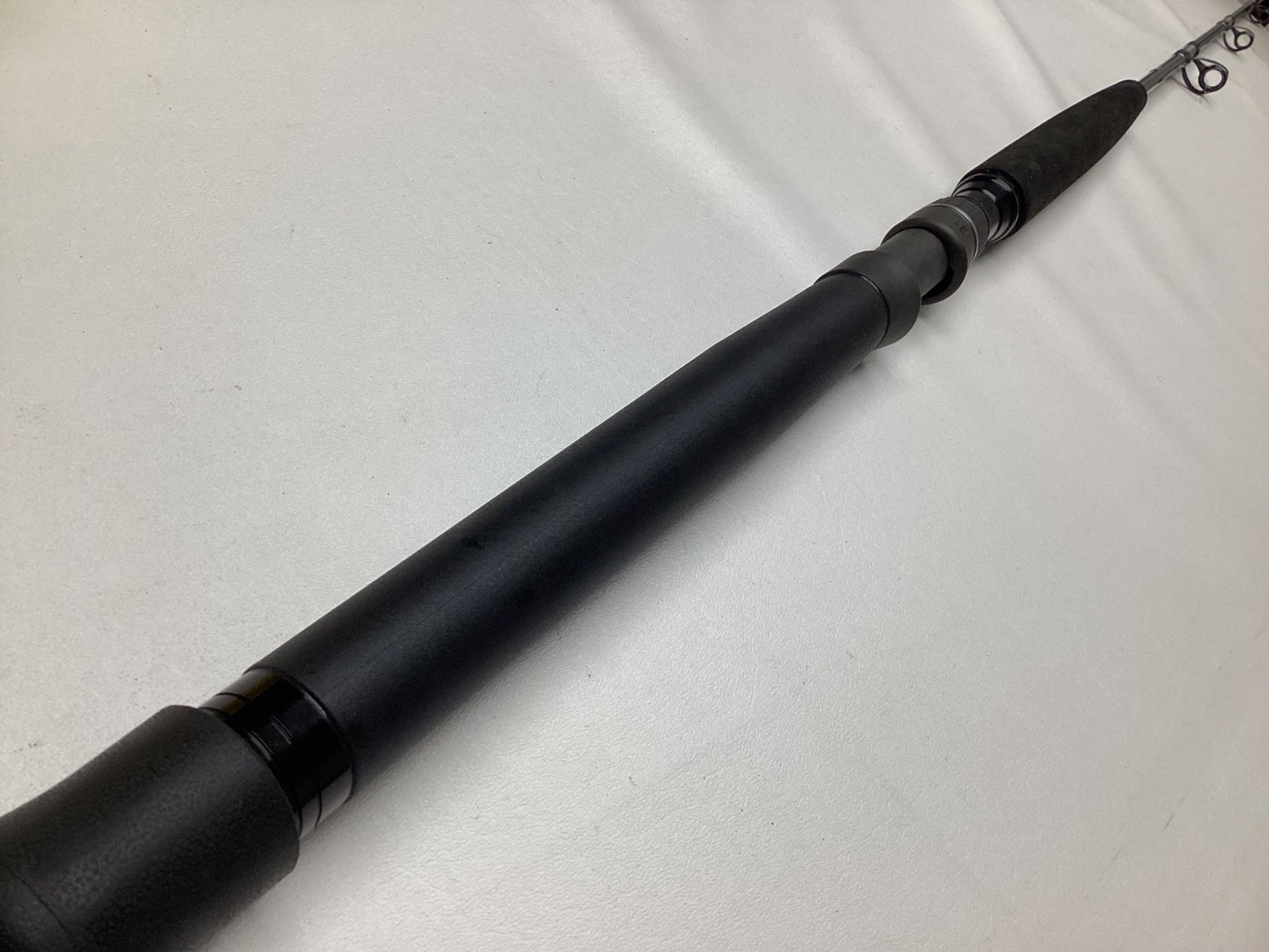 A close-up of a Shimano Terez BW Conventional Slick Butt Rod 6'6" Medium Heavy, in mint condition, is laid diagonally from bottom left to top right on a white surface. Its black finish highlights the textured grip and guide rings, making it ideal for a Rod and Reel Trade-In.