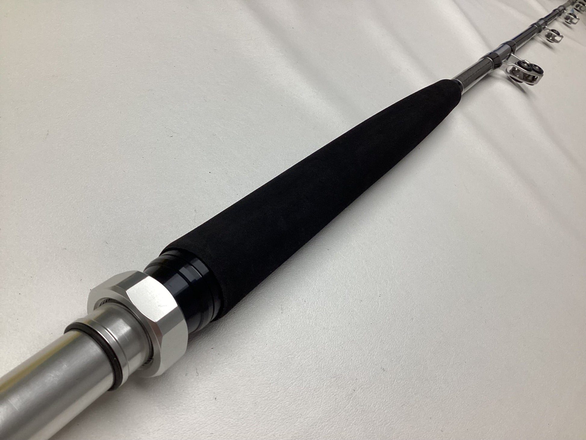 Close-up of a Shimano Terez BW Full Roller Uni Butt Rod 78" Heavy in black, lying on a white surface, with a metal handle and multiple eyelets. Its smooth finish and craftsmanship make it ideal for those interested in our Rod and Reel Trade-In Program or shopping our used gear.