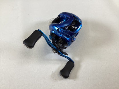 The Daiwa Coastal TWS CLSVTW150HS Used Casting Reel in very good condition features a blue metallic finish, black handles with two large knobs for a firm grip, and is set against a light gray background. It's eligible for the Rod and Reel Trade-In program for store credit.