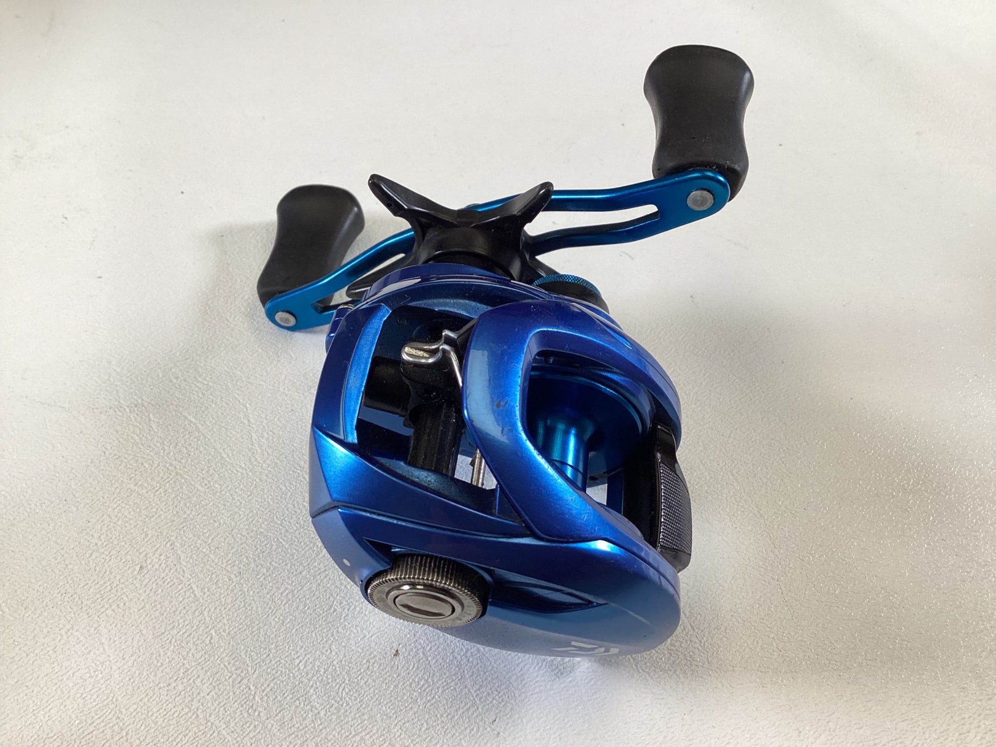 The Daiwa Coastal TWS CLSVTW150HS, a blue baitcasting reel with two black handles, is displayed on a white surface. Its shiny finish and intricate details make it perfect for upgrading through a Rod and Reel Trade-In to receive store credit for used gear. Condition: Very Good. Brand: Daiwa.