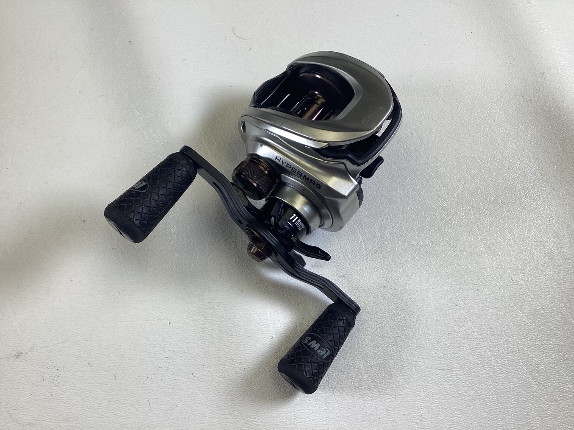 A used Lew's HyperMag TLH1SHG2 7.5:1 RH casting reel in good condition, with dual black textured grip handles, is set against a light gray background. The visible gears highlight precision craftsmanship, ideal for the Rod and Reel Trade-In Program!.