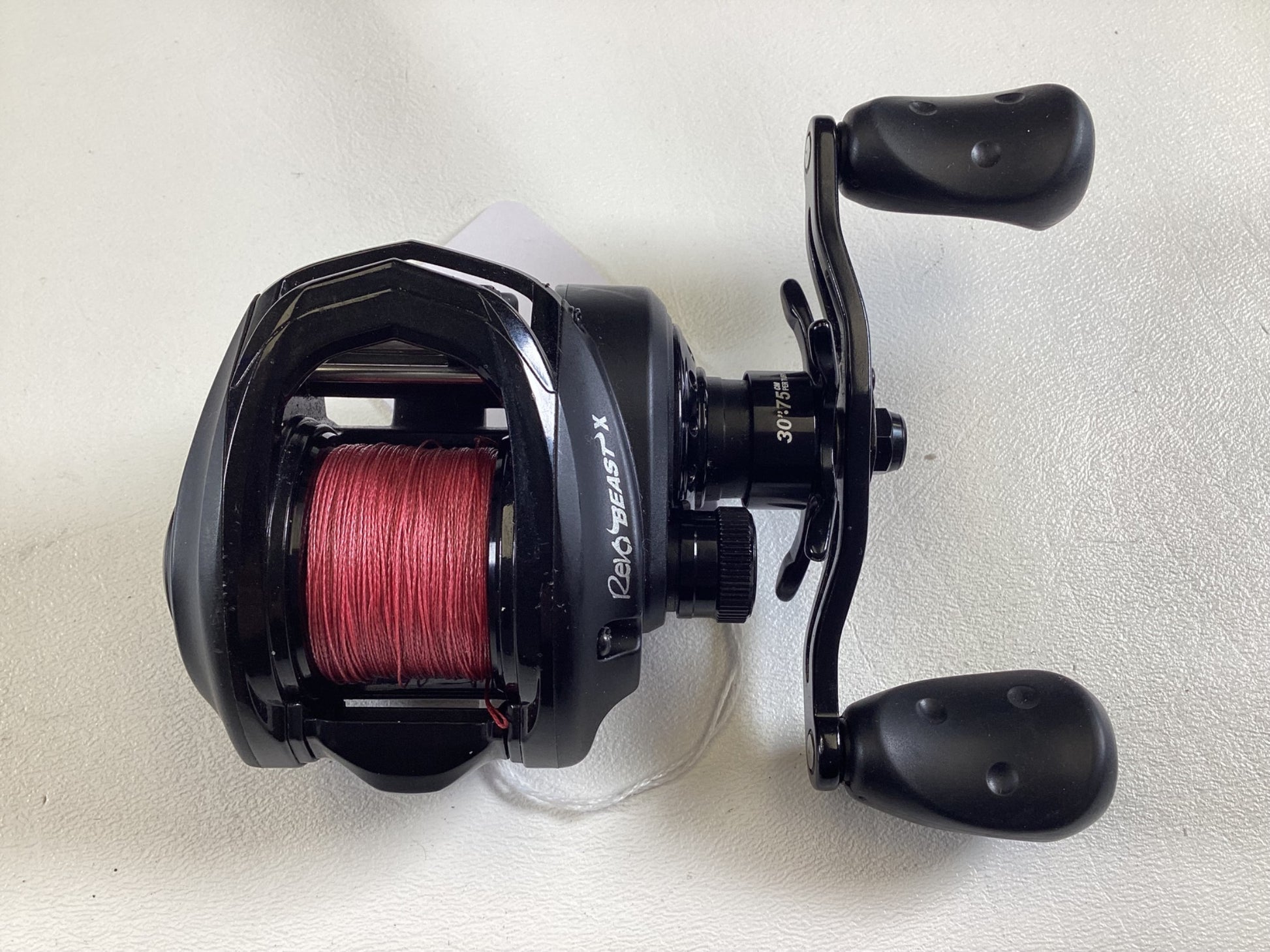 The Abu Garcia Revo Beast X 40 6.4:1 RH, a black baitcasting reel with red line, rests on a white surface. With two large black handles and compact design, it's ideal for anglers ready to upgrade used gear at the Rod and Reel Trade-In event.