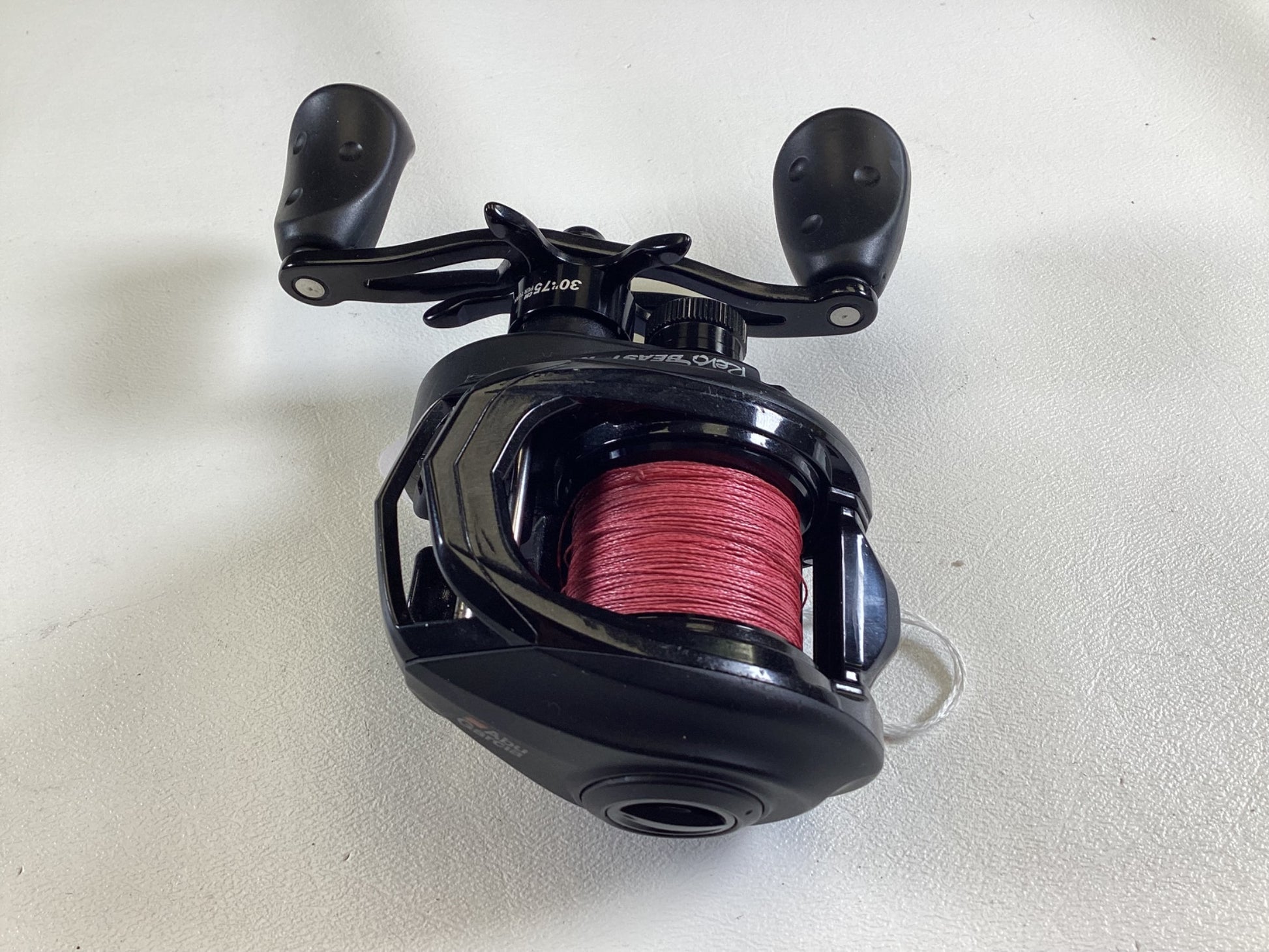 The Abu Garcia Revo Beast X 40 reel with a red line and dual grip handle sits on a white surface, ready for action. Trade in your used gear for store credit and upgrade your next fishing adventure.