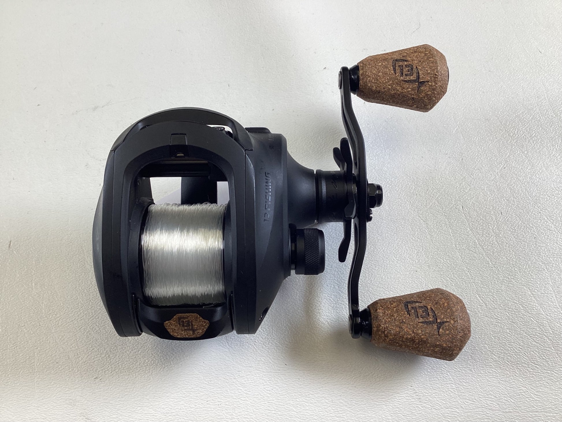 The 13 Fishing Concept A3 Gen II CA3-8.1-RH used casting reel, in excellent condition, is black with cork handles featuring engraved logos. Displayed against a white background, it's wound with translucent line and ready for our Rod and Reel Trade-In program.