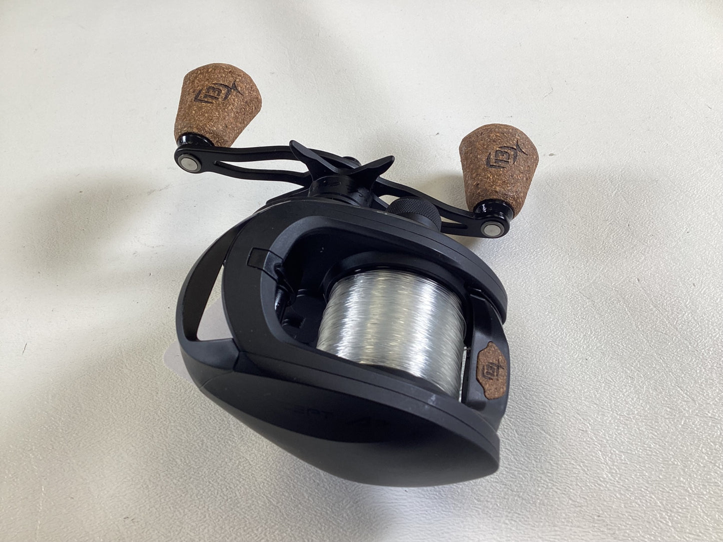 A used 13 Fishing Concept A3 Gen II CA3-8.1-RH casting reel in excellent condition, featuring dual brown cork handles and transparent line, sits on a white surface, perfect for a Rod and Reel Trade-In.