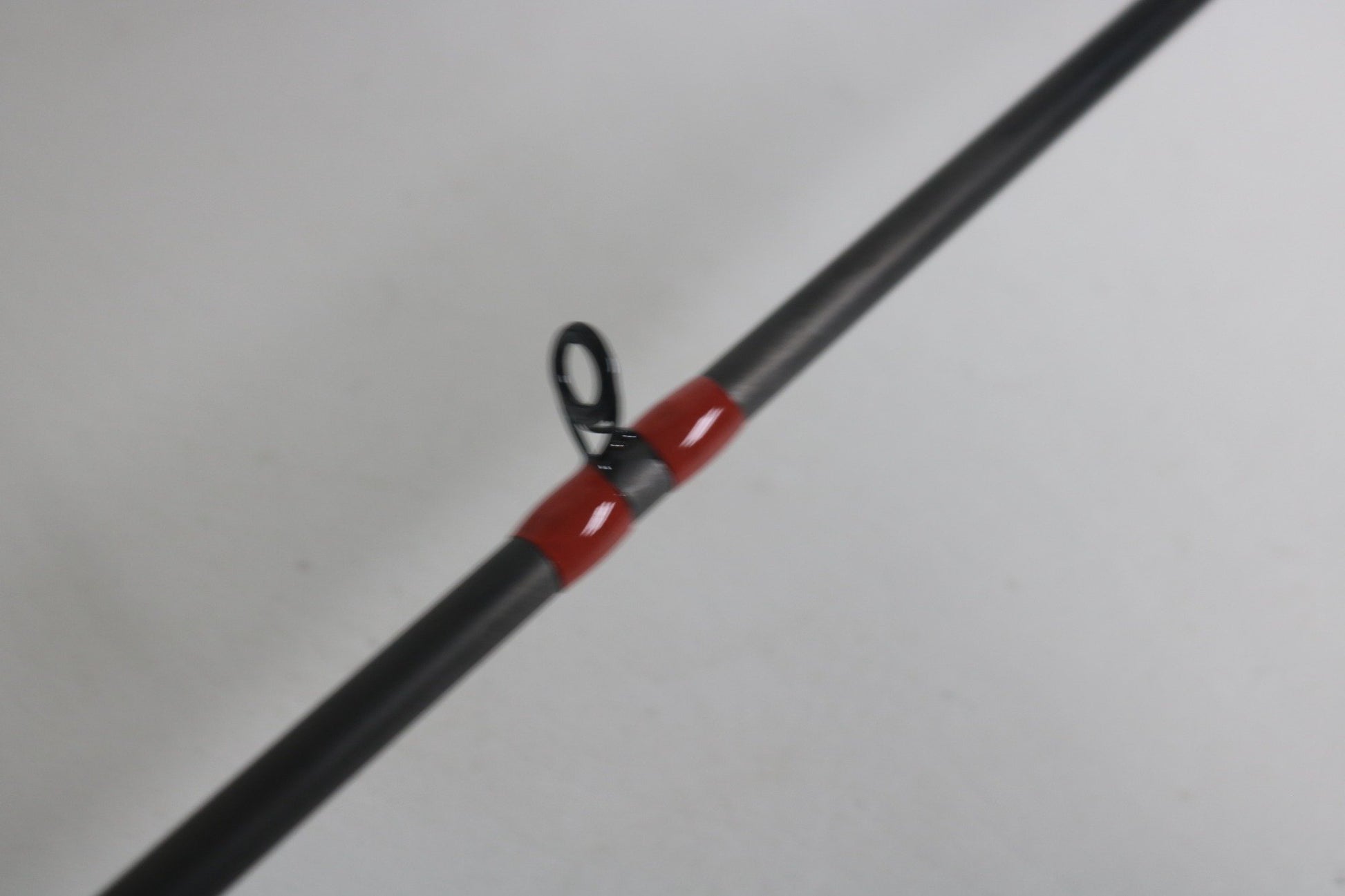 A close-up of the G. Loomis GCX 783C MBR casting rod showcases a guide ring on its dark surface with red wrappings. Set against a plain, light background, it's ideal for evaluating its excellent condition before deciding on the Rod and Reel Trade-In Program.