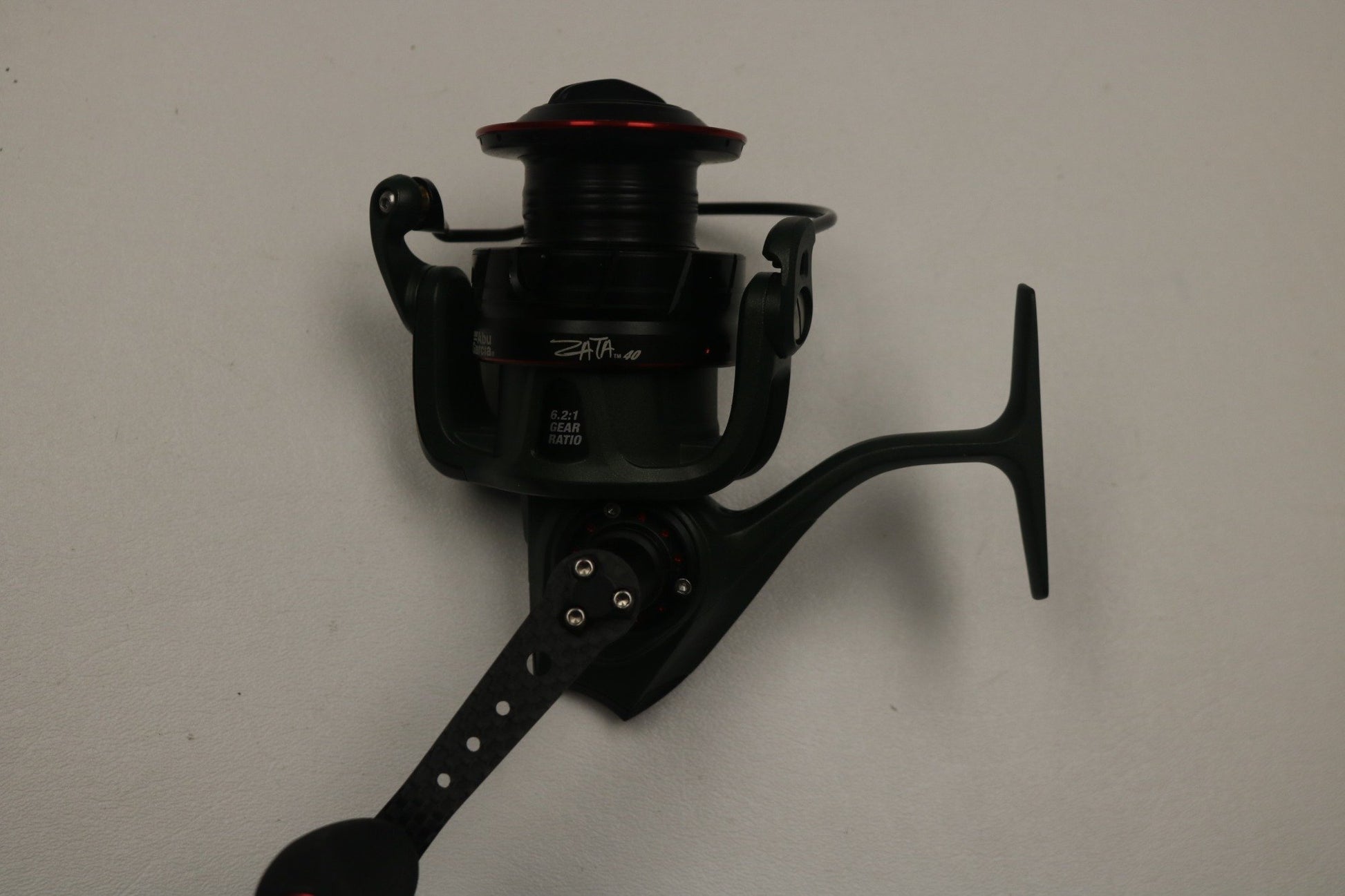 Close-up of Abu Garcia's used Zata ZATASP40 spinning reel in excellent condition, showcasing its slick black design with red accents on a handle against a white background. Consider trading your used gear for store credit through our Rod and Reel Trade-In Program.