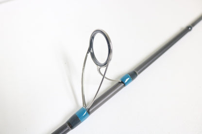 Close-up of a Megabass Cookai Gulf CKG-70M+S 7'0" spinning rod guide with a metal loop and blue-black attachments. The gray rod pops against the white background, ideal for our Rod and Reel Trade-In Program offering store credit for your used gear.