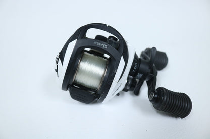 The Quantum Accurist PT 7.0:1 Casting Reel in black and white, featuring ergonomic handles and compact design, sits on a white surface with a spool of fishing line. Ideal for our Rod and Reel Trade-In Program, this quality used gear is in very good condition.