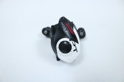 A small, black-and-white Quantum Accurist PT casting reel with two wheels is seen from above on a white surface. It has a central black circle and a red accent on top, offering precision akin to the finest gear used in the Rod and Reel Trade-In Program.