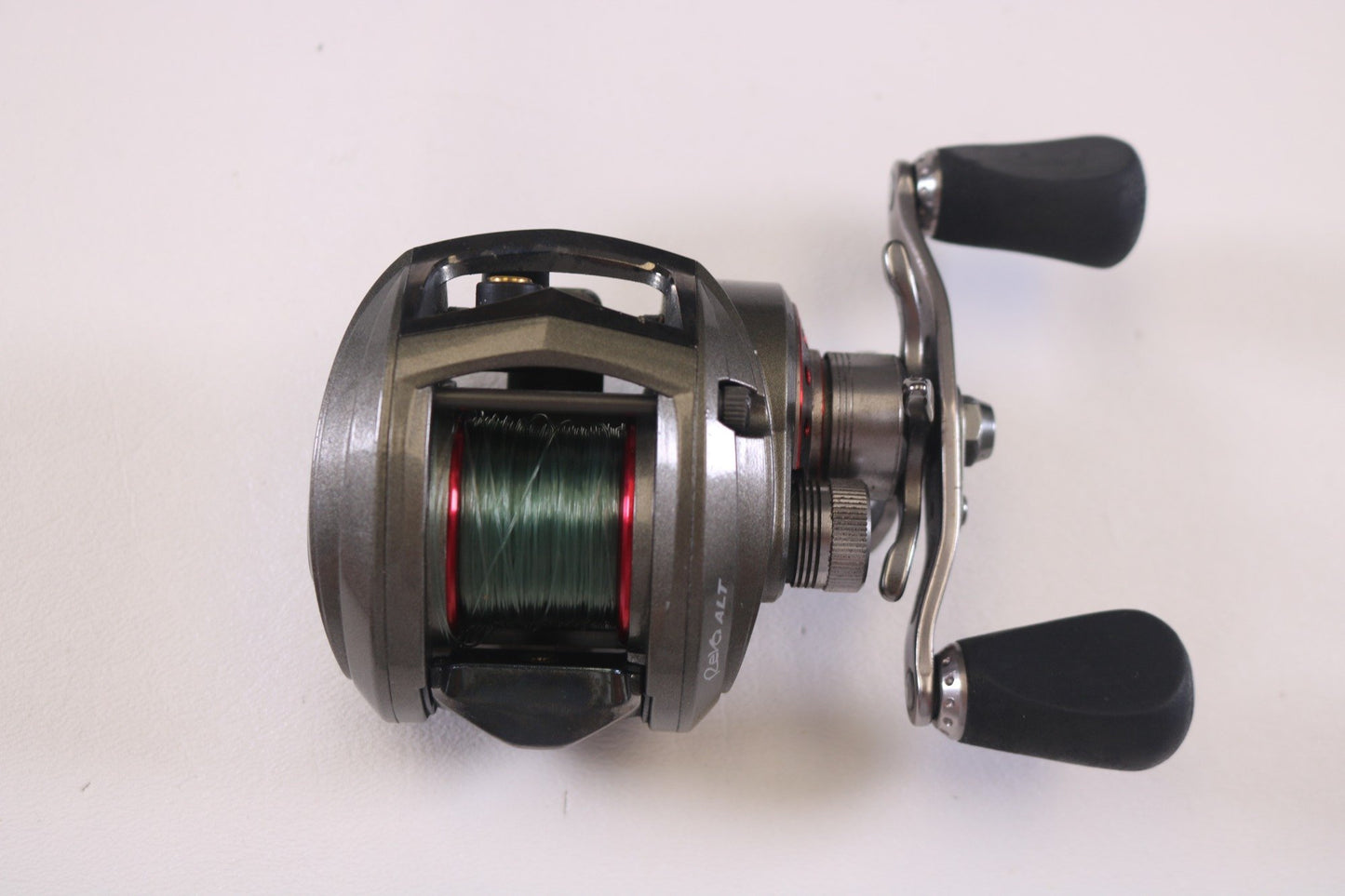 The Abu Garcia Revo ALT 6.4:1 RH, a used casting reel in very good condition, features a silver finish with a black handle and spool wound with green line. It's ideal for our Rod and Reel Trade-In Program against a plain white backdrop.