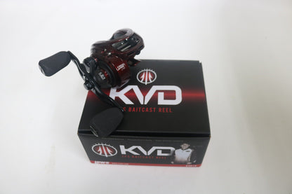 A maroon Lew's KVD1H baitcast reel rests on its sleek black box with the bold KVD logo and an angler image. Ideal for upgrading via our Rod and Reel Trade-In Program, this used reel in very good condition has a 6.2:1 ratio and two sturdy black rubber handles.