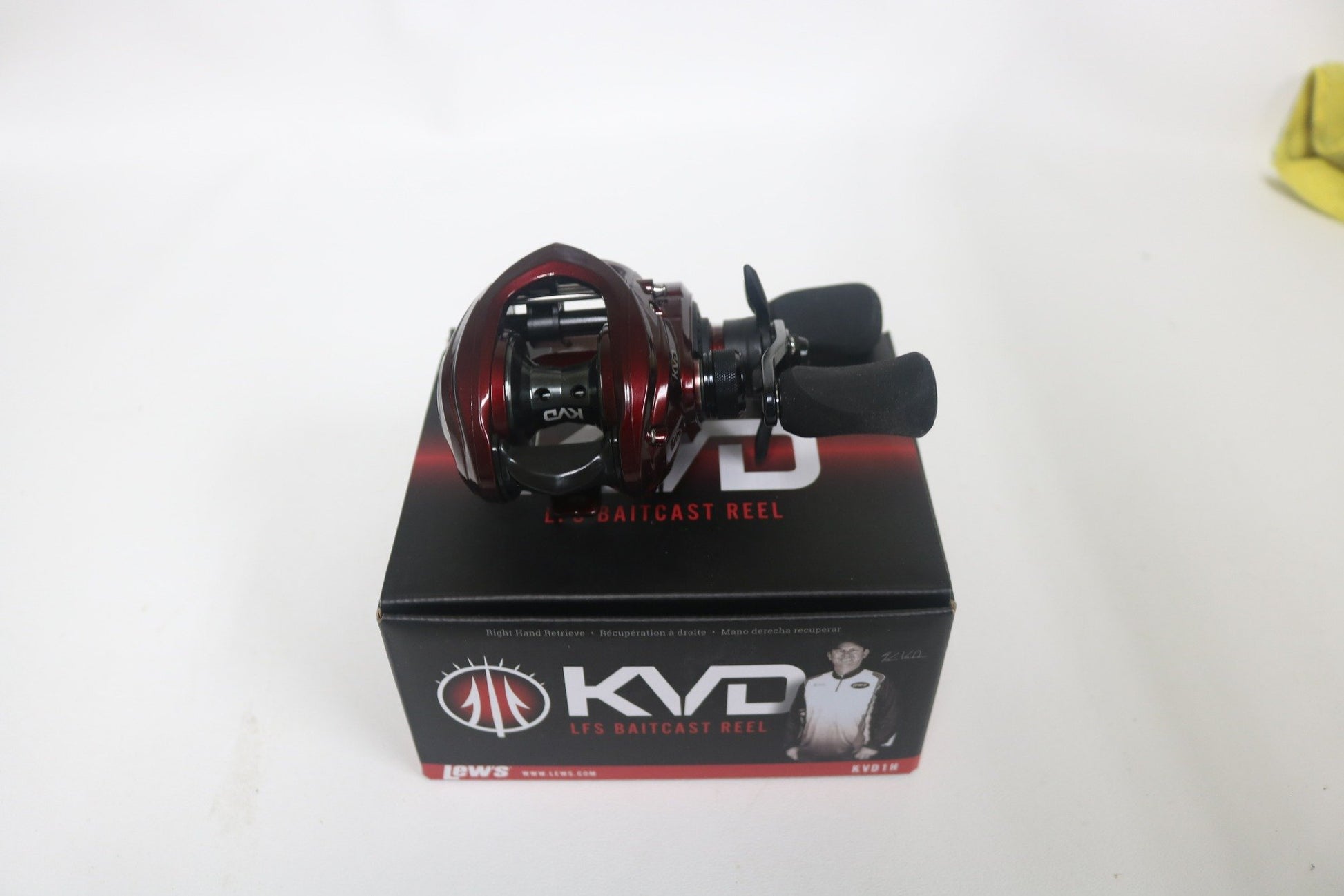 A red and black Lew's KVD KVD1H 6.2:1 right-hand baitcast reel, in very good used condition, sits atop its box. With dual handles and visible internal components, it’s perfect for anglers participating in our Rod and Reel Trade-In Program to upgrade their gear.