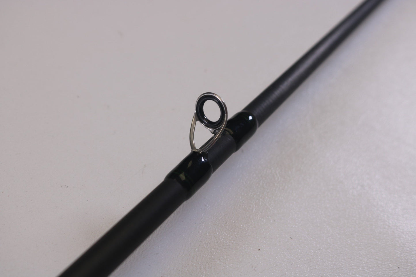 Close-up of a Shimano Curado CDC610M 6'10" Medium casting rod, in excellent condition, featuring a single circular line guide. Perfect for the Rod and Reel Trade-In Program, it rests on a light gray surface, highlighting its sleek design.