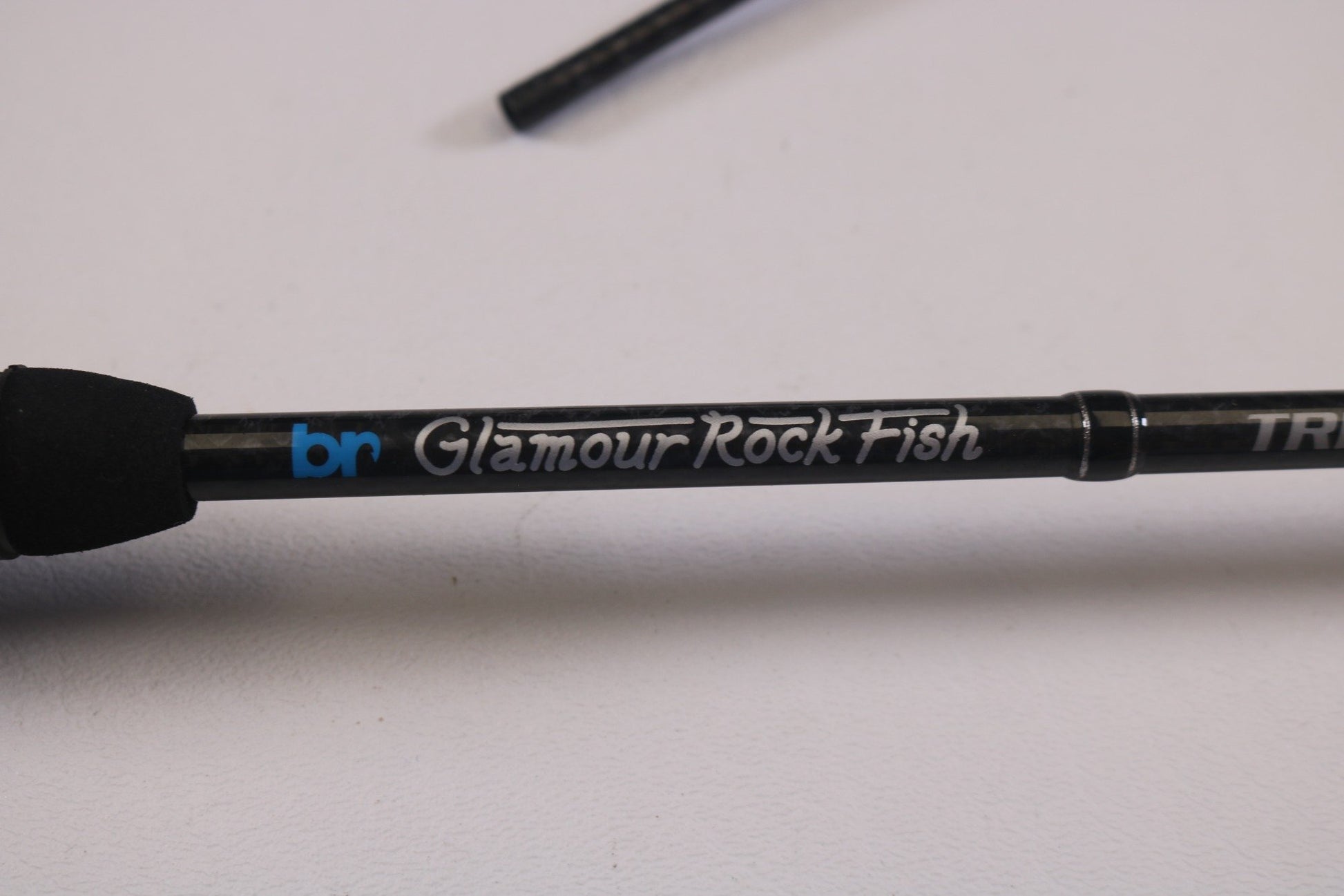 Close-up of a Breaden Glamour Rockfish Trevalism Kabin 506 TS-tip 5'4" Ultra Light, featuring "Glamour Rock Fish" in white on black. Ideal for Rod and Reel Trade-In participants, this used rod is in excellent condition and displayed elegantly on a plain white surface.