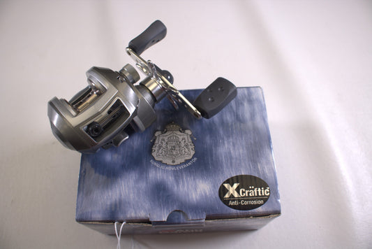 The Abu Garcia Revo S-L Gen 1 6.4:1 LH Used Casting Reel, in excellent condition, features a metallic finish on black-gripped handles. It rests atop a blue box with an emblem and "X-Crattic Anti-Corrosion" sticker. Ideal for the Rod and Reel Trade-In Program to upgrade gear for store credit.