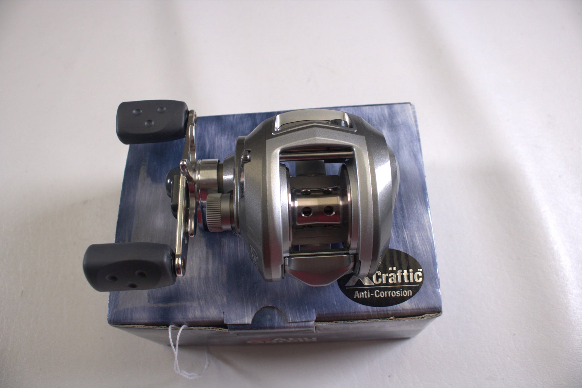 A gray Abu Garcia Revo S-L Gen 1 baitcasting reel with black handles is showcased on a "Crattic Anti-Corrosion" box against a white background, as part of our exclusive Rod and Reel Trade-In Program.