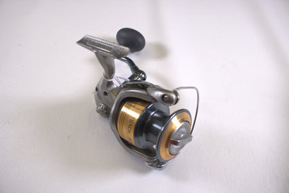 A close-up image of a Shimano Stradic ST8000FI fishing reel with a silver body and gold spool. The sleek, modern design features a black handle on a white surface—ideal for those trading in gear via the Rod and Reel Trade-In Program to earn store credit, even with fair condition items missing parts.