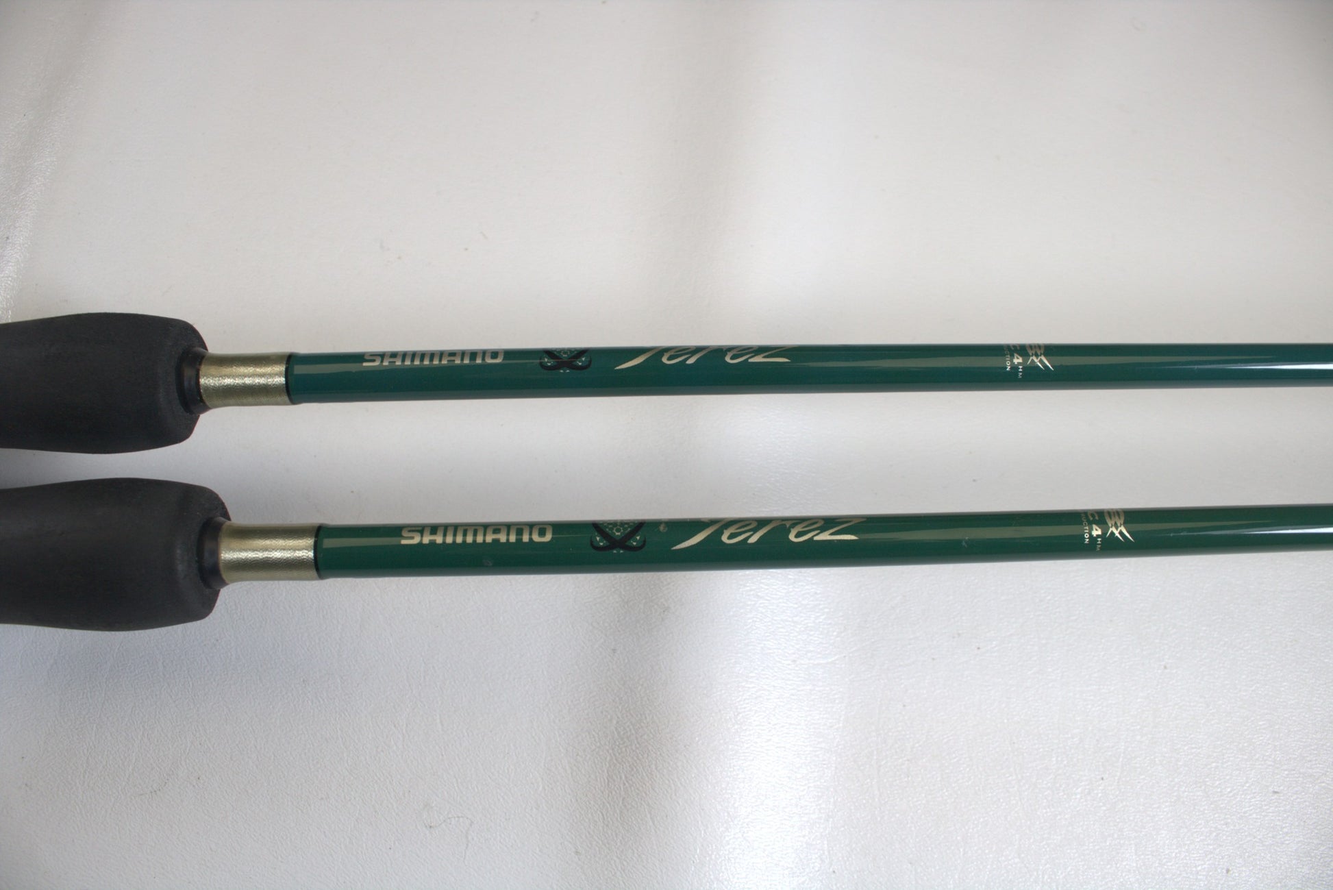 Two Shimano Terez Evergreen 7'2" Medium Light spinning rods with black grips are shown. The rods, in good condition and featuring cursive branding, lie parallel on a white background.