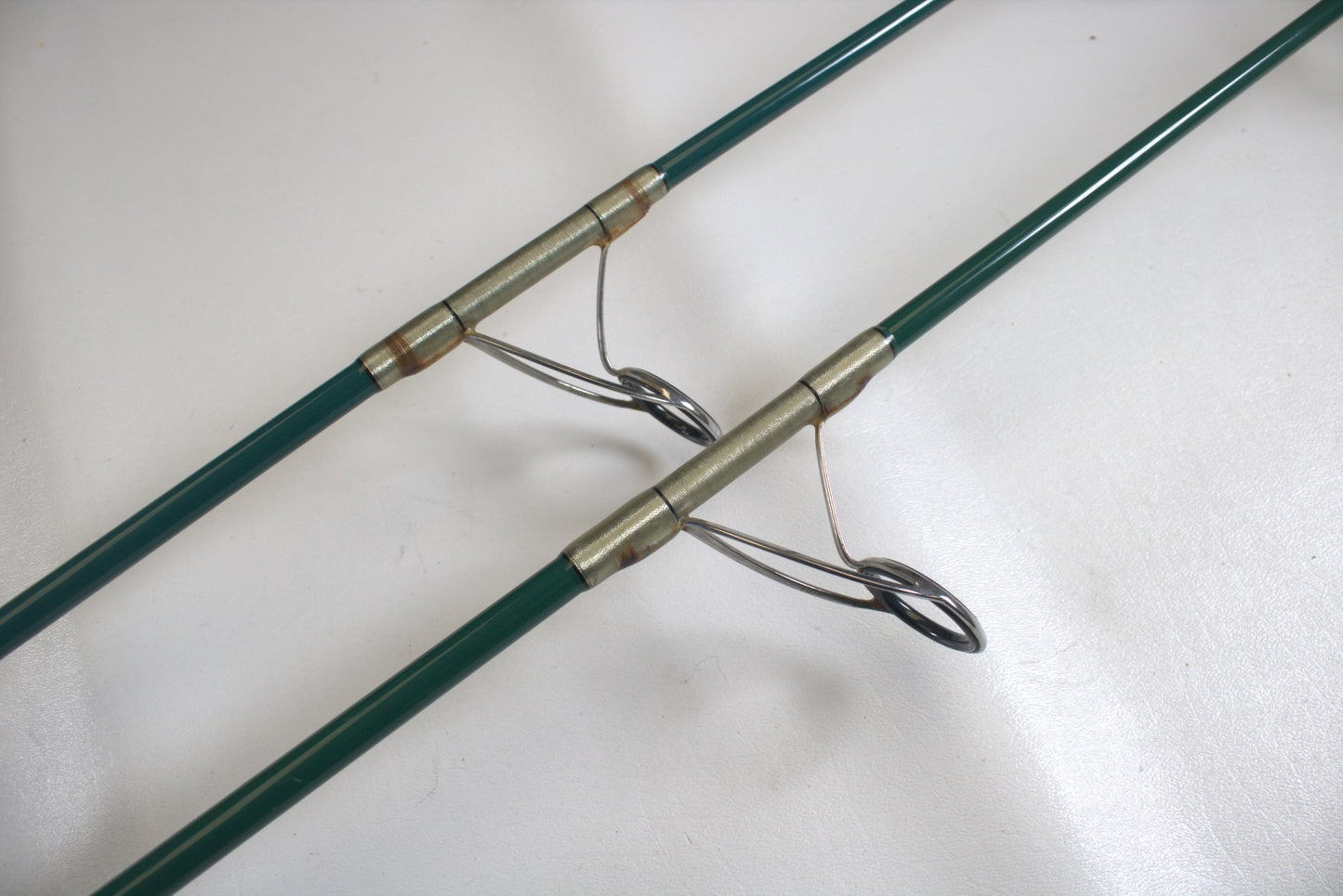 Close-up of two Shimano Terez Evergreen TZS-72ML 7'2" Medium Light used spinning rods in good condition on a white surface, showing metal eyelets, guides, and bindings arranged parallel.