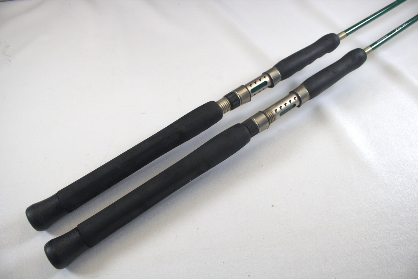 Two Shimano Terez Evergreen TZS-72MH rods, each 7'2" with black handles and silver reel seats, lie parallel on a white surface. They angle diagonally toward the top-right corner, showcasing their full length.