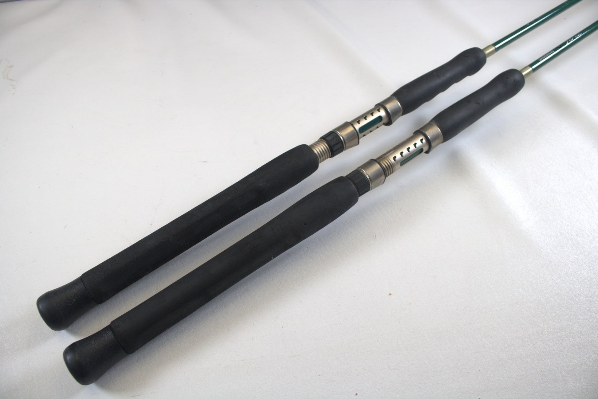 Two Shimano Terez Evergreen TZS-72MH rods, each 7'2" with black handles and silver reel seats, lie parallel on a white surface. They angle diagonally toward the top-right corner, showcasing their full length.