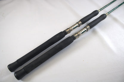 Two Shimano Terez Evergreen spinning rods, models TZS-72MH and TZS-72M in good condition, lie parallel on a light surface. They feature black handles with metallic reel seats and greenish shafts, showcasing a sleek and modern design.