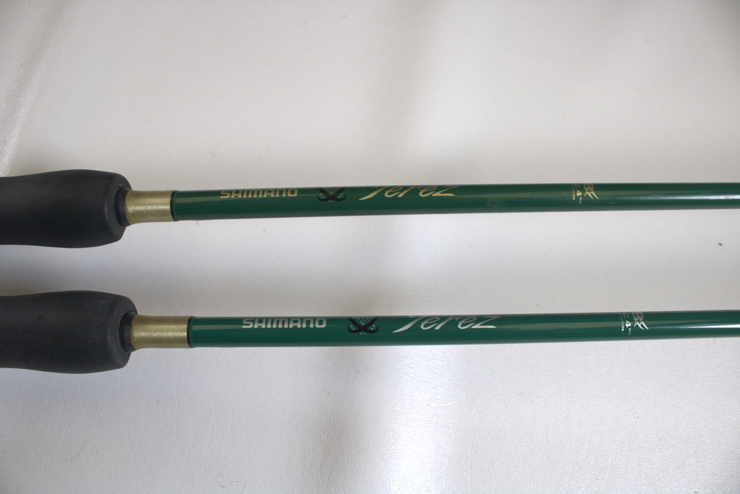 Close-up of two Shimano Terez Evergreen spinning rods, TZS-72MH and TZS-72M models, with green shafts and black grips, printed with "Shimano" in gold. They are parallel on a white surface.