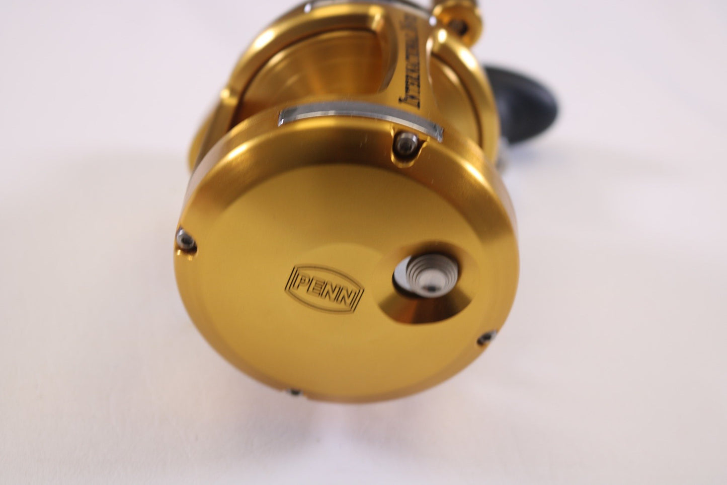 A close-up showcases the gold Penn International VI INT16VIS 5.2:1/1.6:1 RH casting reel in mint condition, featuring a round design with "Penn" engraved on its side, perfect for our Rod and Reel Trade-In Program. The gently used reel's handle peeks from the background against a white surface.