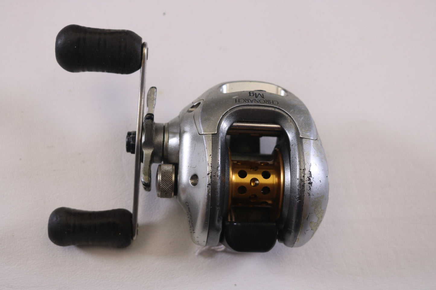 The Shimano Chronarch 51Mg 6.2:1 LH, a used casting reel with silver finish, black handles, and honeycomb-style spool, is perfect for upgrading your gear or a rod and reel trade-in to earn store credit.